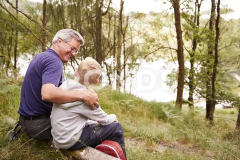 Grandfather and grandson on a hike sitting on a fallen tree in a forest, look Stock Photos