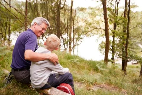 Grandfather and grandson on a hike sitting on a fallen tree in a forest, look Stock Photos
