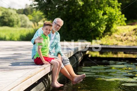 Grandfather and grandson sitting on river berth Stock Photos