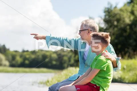 Grandfather and grandson sitting on river berth Stock Photos