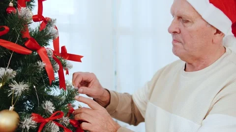 Grandfather decorate a Christmas tree, adding ribbons and ornaments in their Stock Footage 319048628