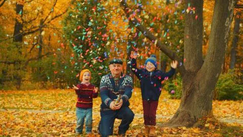 Grandfather is exploding party cracker in the autumn park with his grandsons Stock Photos