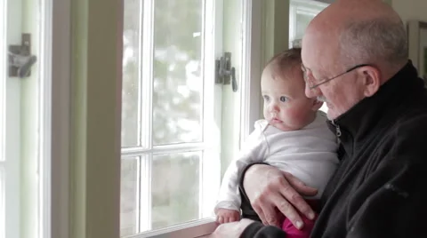 Grandfather holding his granddaughter near window Stock Footage