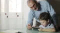 grandfather is learning from his grandson how to use a tablet to surf in web HD Footage