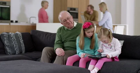 Grandfather plays game on electronic tablet with grand daughters in beautiful Stock Footage 50853955