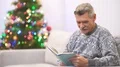 The grandfather read a book and take a gift from a girl near the christmas tree 4k or 4k+ Resolution