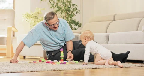 A grandfather sets up a tower of blocks on the living room carpet for grandson Vidéo 156637726