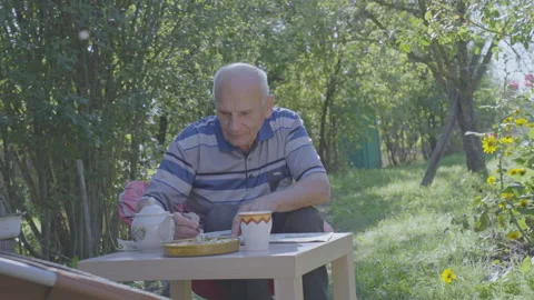 Grandfather solves crossword puzzle while sitting at table in garden Stock Footage 253182780