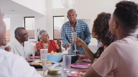 Grandfather standing at the dinner table proposing a toast during a family Stock Footage 106694413