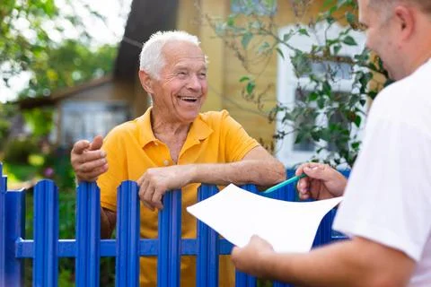 Grandfather talking to census agent standing at fence of his country house Stock-Fotos