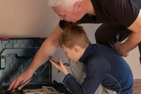 Grandfather teaches grandson neatly stack in suitcase an electric a screwdriver. Stock Photos