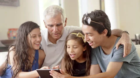 Grandfather using a tablet computer with grandchildren in living room Vidéo 49188997