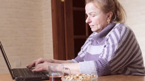 Grandma chatting behind the laptop while sitting in the kitchen Video stock 88209770