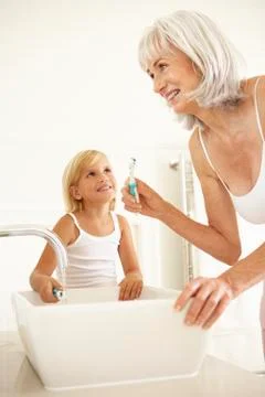 Grandmother Brushing Teeth In Bathroom With Granddaughter Watching Stock Photos