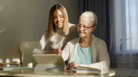 Grandmother Learning Digital Tablet with Help of Young Woman Vidéo 103364402