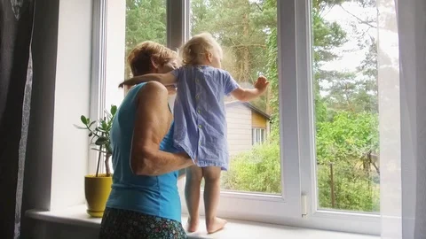 Grandmother playing and taking care of child at home. looking through the win Stock Footage