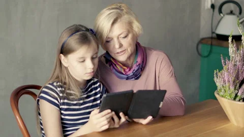 Grandmother reading something on e-book with her young granddaughter at home,4K Видео 148832190