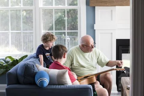 Grandpa Fixes Guitar Strings While Teen and Preschool Grandsons Watch Foto stock