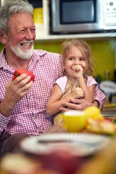 Grandpa laughing out loud with his granddaughter in his lap, sitting in the k Stock Photos