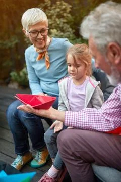 Grandpa showing boat made from paper to his granddaughter while grandma is wa Stock Photos