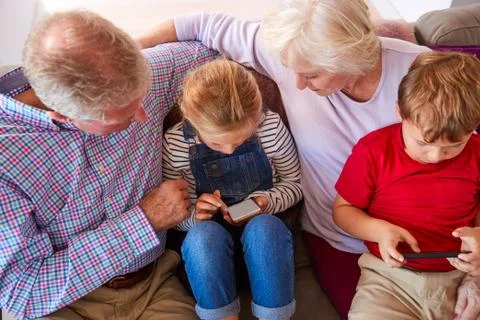 Grandparents Playing Video Games With Grandchildren On Mobile Phones At Home Stock Photos