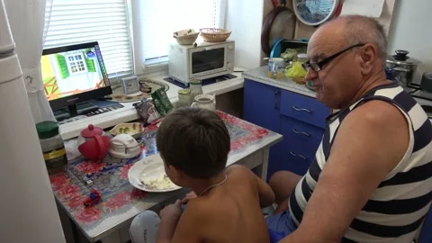 Grandson eats Russian cream cheese in kitchen watching TV with grandad sitti Stock Footage 137583594