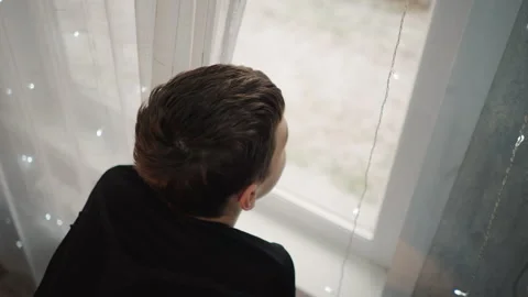 Grandson looking out over backyard with hopeful tilt of head, morning light Stock Footage 334789530
