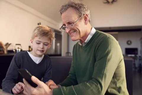 Grandson Showing Grandfather How To Solve Problem And Use Mobile Phone At Home Stock Photos