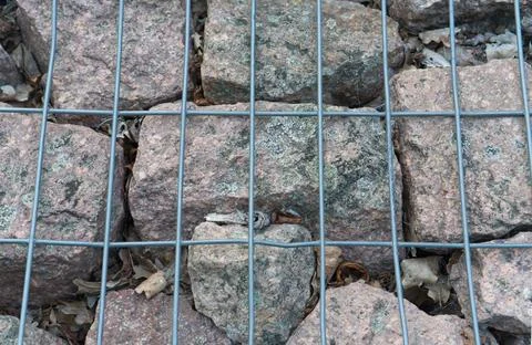 Granite cobblestone pavement texture viewed behind a metal wire mesh grid Stock Photos