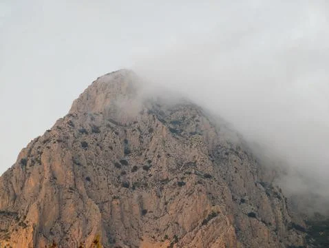Granite peak under cloudy sky, Moody rocky summit displaying warm hues and Stock Photos