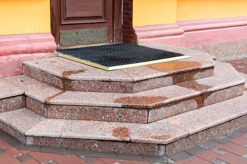 Granite steps of stone threshold with rubber foot mat at wooden entrance. Stock Photos