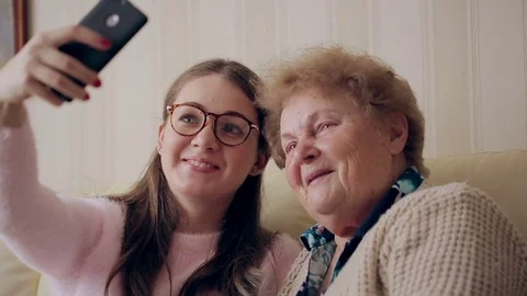 Granny and young girl making self photos on mobile or smart phone while sitting Stock Footage