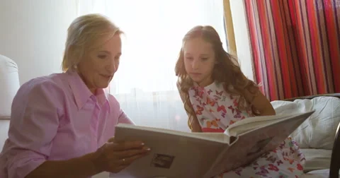 Granny sitting on couch next to her granddaughter and looking through photo Stock Footage 66286327