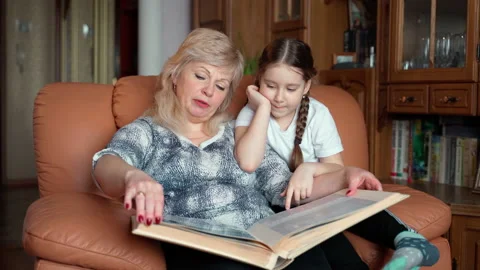 Granny sitting on couch next to her granddaughter and looking photo album Stock Footage 152709954