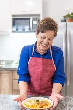 Granny smiling serving soup in the kitchen Stock Photos