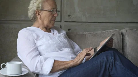 Granny using a digital tablet while sitting on couch Stock Footage 54661712