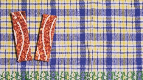 Granola bars move one after another on a beautiful tablecloth, view from above Stock Footage 126379112
