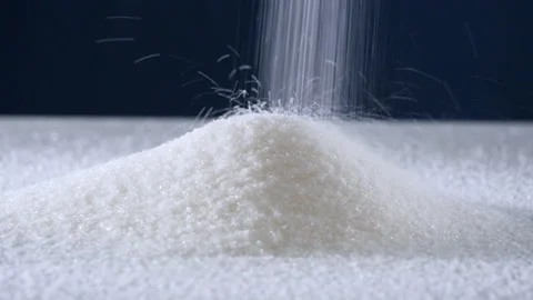 Granulated sugar streams down on a white table on a blue background 库存影片 178445426