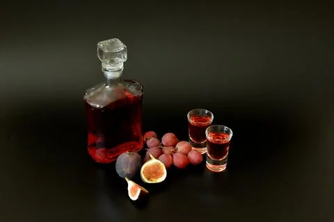 Grape-fig liqueur in a bottle and two glasses on a black background, next t.. Stock Photos