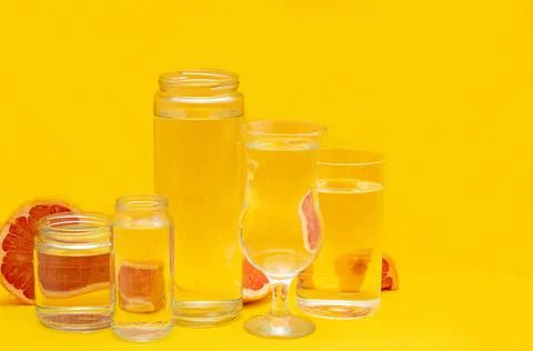 Grapefruit distorted through glasses with water. Summer concept. Yellow backg Stock Photos