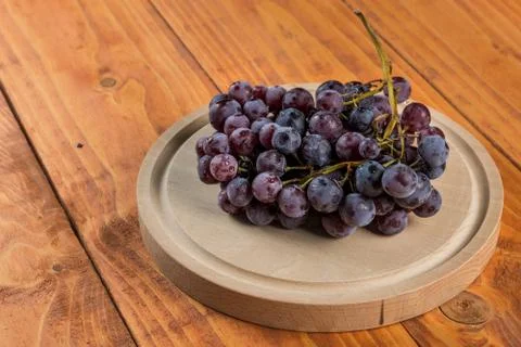 Grapes on the round wooden kitchen board on the table Stock Photos