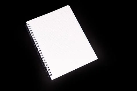 Graph paper notebook with spiral binding, positioned diagonally against black Stock Photos