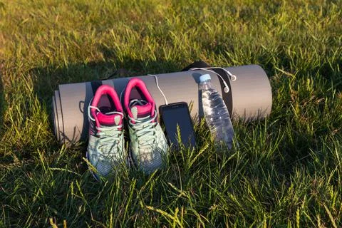 On the grass there are tools for training, yoga Mat, sneakers, phone, headpho Stock Photos