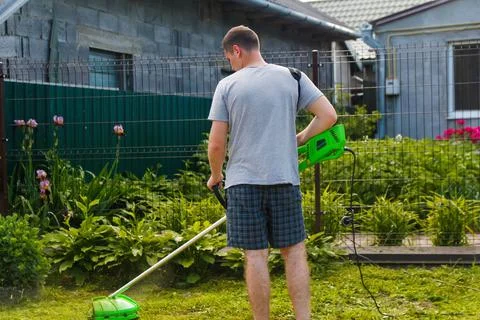 Grass trimmer. Back view of a man mowing the grass. Outdoor view of young wor Stock Photos
