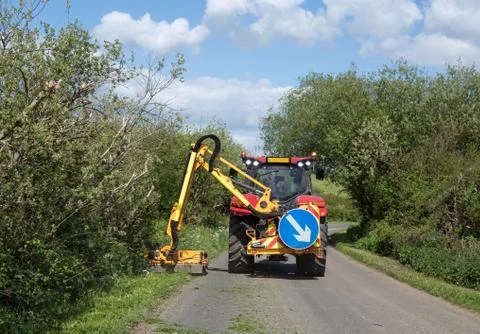 Grass verges being cut by large tractor mower in Sussex country lane during S Stock Photos