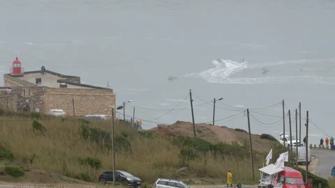 Grassy cliff with lighthouse and pro surfer riding tall waves in ocean Stock Footage 157700713