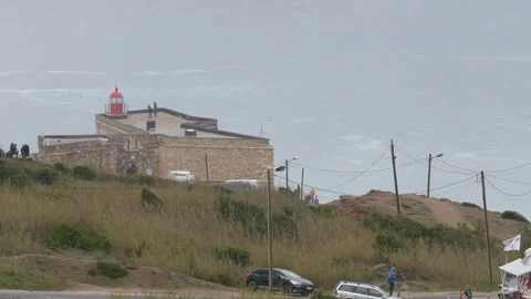 Grassy cliff with red lighthouse and pro surfer riding tall waves in ocean Video stock 157700740