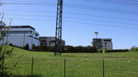 A grassy field with dandelions in front of modern buildings and a power pole. Ov Stock Footage 309331460