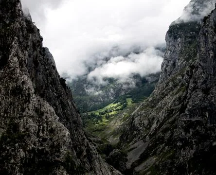 Grassy Field Lit Between Two Cloudy Mountains Stock Photos