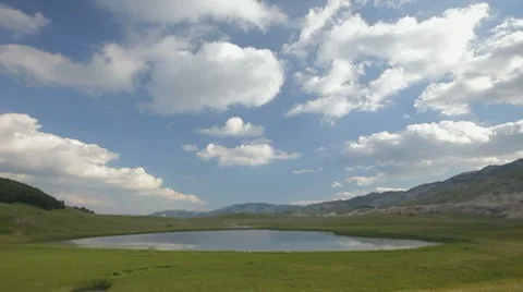Grassy glade with a small lake.White clouds passing across blue sky. Stock Footage 8562068
